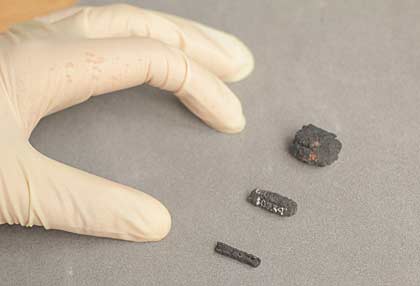 a hand next to three small beads made of a dark grey coal-like substance