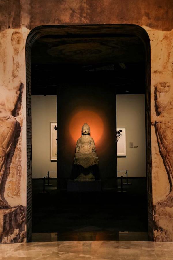 展览入口,一尊唐代佛坐像,国家一级文物,高199、宽79.5、厚67厘米,征集; 坐像和台座为系整体雕刻而成,肉髻表面遍布波状发纹,正面作“品”字形。右手残失,左手食指、中指伸直。衣褶在膝前向下弯曲,袈裟下摆垂覆于八角形台座上。