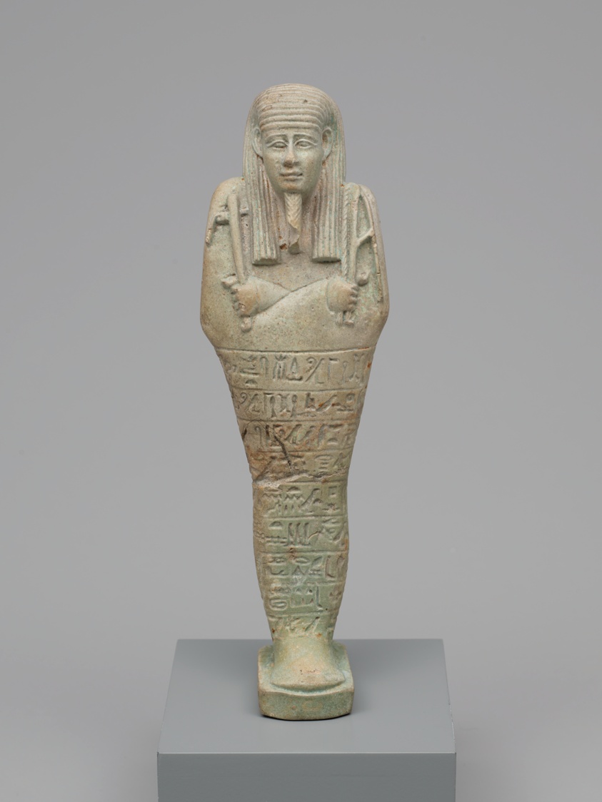 巫沙布提俑（丧葬雕像），第三十王朝晚期（公元前380-前343年），古埃及 作为为葬礼制作的数百件几乎相同的物品之一，小巧的“巫沙布提俑”持有镐、锄头和一袋种子，以便继续为它来世的主人（一个名为horudja的牧师）农业劳作。